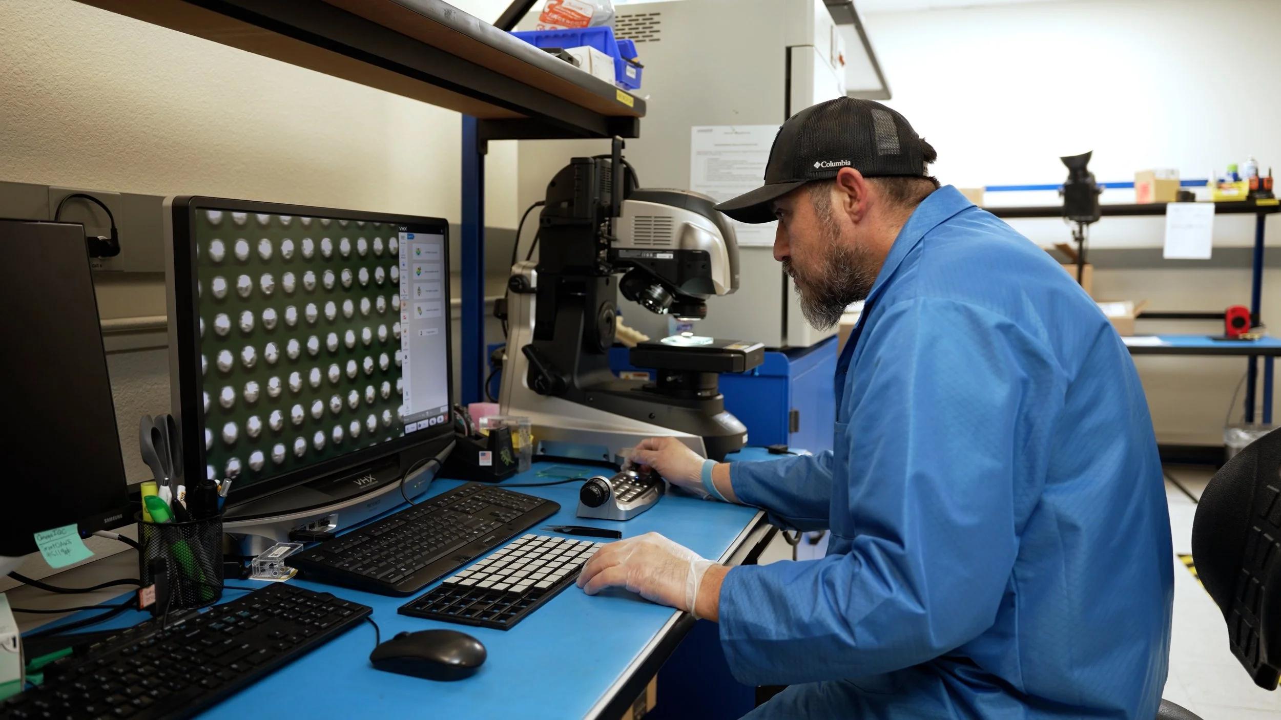 Omega GTI technician inspecting components on a Keyence digital microscope in the test and inspection lab
